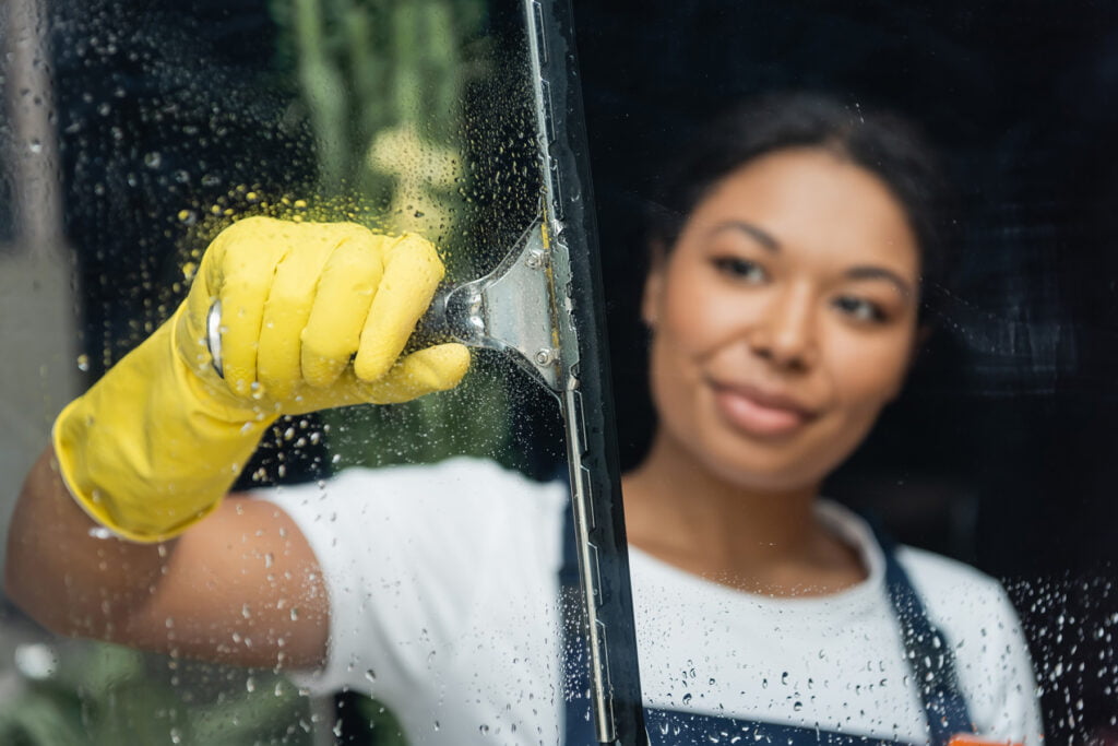 blurred woman in rubber glove cleaning glass with window wiper